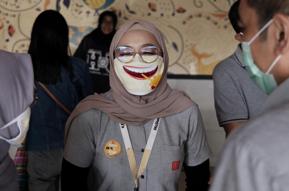 An employee wearing a face mask as a precaution against the new coronavirus outbreak shares a light moment with colleagues at a McDonald's restaurant in Jakarta, Indonesia, Sunday, May 10, 2020. (AP Photo/Dita Alangkara)