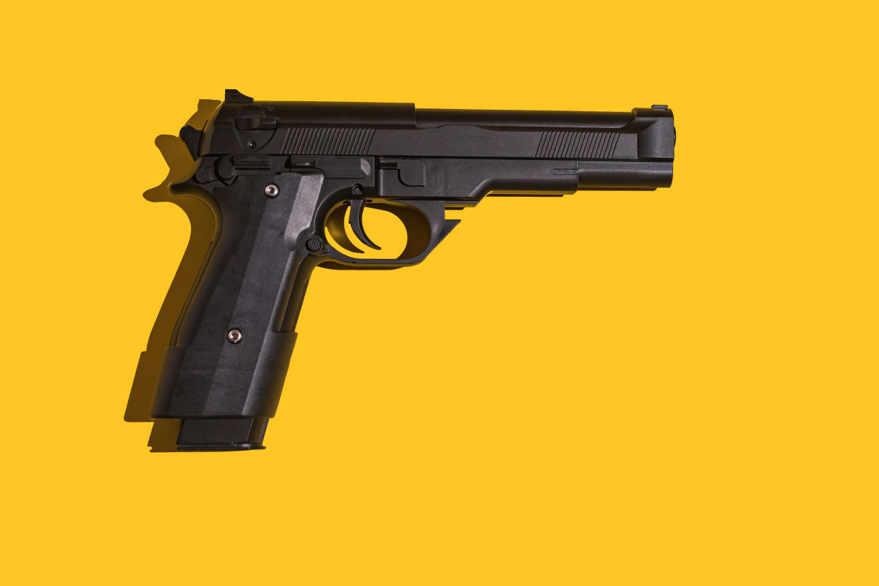 Black gun with direct light and hard shadow on yellow background. 