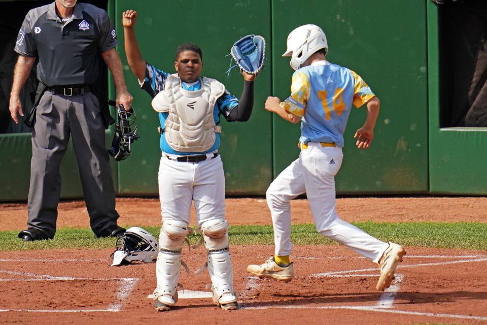 El Segundo, Calif.'s Brody Brooks (14) scores the second of two runs as Curacao's Yaedon Lourens Martie waits for the late relay throw, on a double by Lucas Keldorf during the first inning of the Little League World Series Championship game in South Williamsport, Pa., Sunday, Aug. 27, 2023. (AP Photo/Tom E. Puskar)