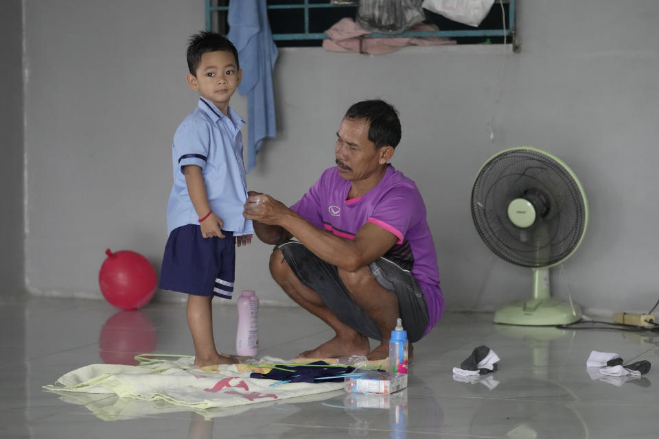 Tawee Lasopha helps his grandson Thanathorn Sopha, son of his daughter Maliwan Lasopha who was killed in a knife and gun attack at The Young Children's Development Center, get dressed as he goes to school in the rural town of Uthai Sawan, in Nong Bua Lamphu province, northeastern Thailand, Thursday, Oct. 5, 2023. On Friday, Oct. 6, Tawee marks the first anniversary of the death of his daughter Maliwan Lasopha. (AP Photo/Sakchai Lalit)