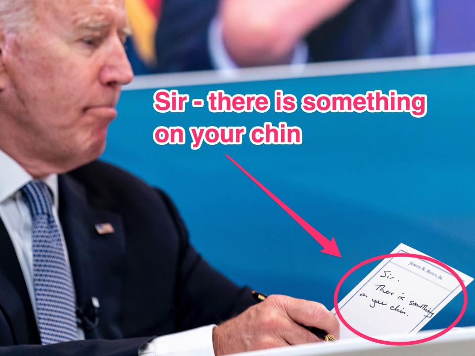 President Joe Biden holds a card handed to him by an aide that reads "Sir, there is something on your chin."