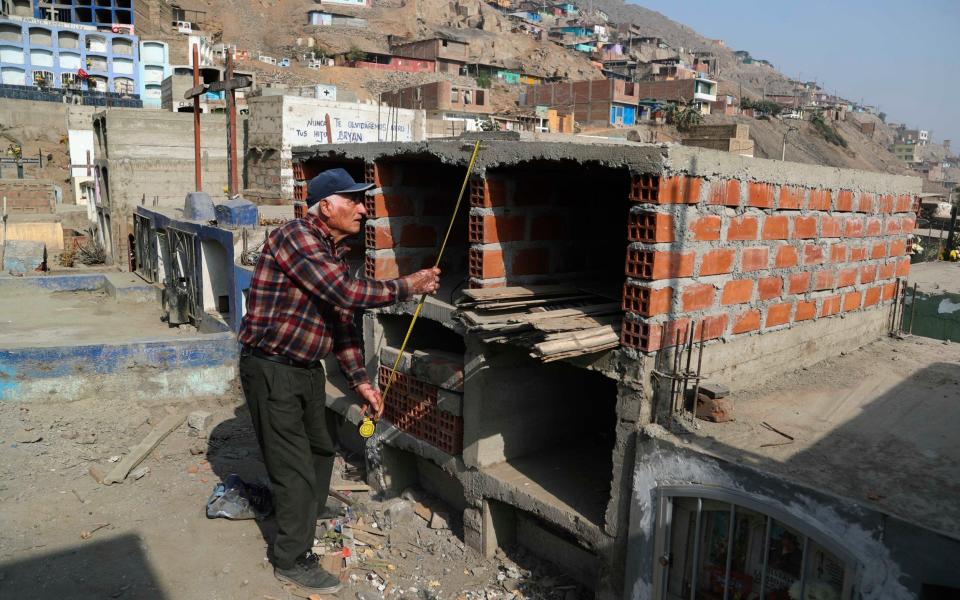 Victor Coba takes measurements of the tombs he's building for his family at San Lazaro cemetery on the outskirts of Lima, Peru - Martin Mejia/AP