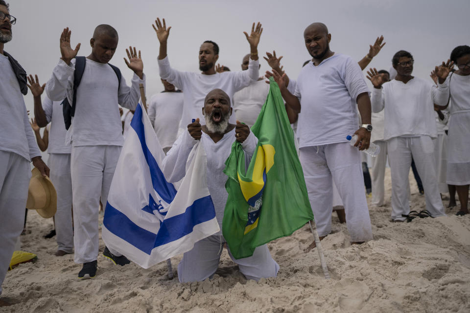 Baptist bishop Wedson Tavares holds flags of Brazil and Israel as he blesses elected officials from city councilors on up to President Jair Bolsonaro, in an area of the Abaete dune system, at a steep rise of sand evangelicals call the "Holy Mountain", in Salvador, Brazil, Sunday, Sept. 18, 2022. This year there are nearly 500 evangelical pastors running for state and federal legislatures, more than triple the number in 2014, according to data from political scientist Bruno Carazza. (AP Photo/Rodrigo Abd)