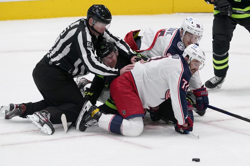 Linesmen Pierre Racicot (65), Dallas Stars center Radek Faksa (12), Columbus Blue Jackets' Nick Foligno, front, and Jack Roslovic, rear, fall to the ice after a face off by Faksa and Foligno in the second period of an NHL hockey game in Dallas, Saturday, March 6, 2021. (AP Photo/Tony Gutierrez)