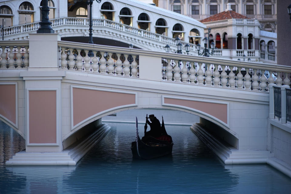A gondolier steers his boat beneath a quiet pedestrian walkway at the Venetian hotel and casino in Las Vegas, Feb. 4, 2021. The toll of the coronavirus is reshaping Las Vegas almost a year after the pandemic took hold. The tourist destination known for bright lights, big crowds, indulgent meals and headline shows is a much quieter place these days. (AP Photo/John Locher)