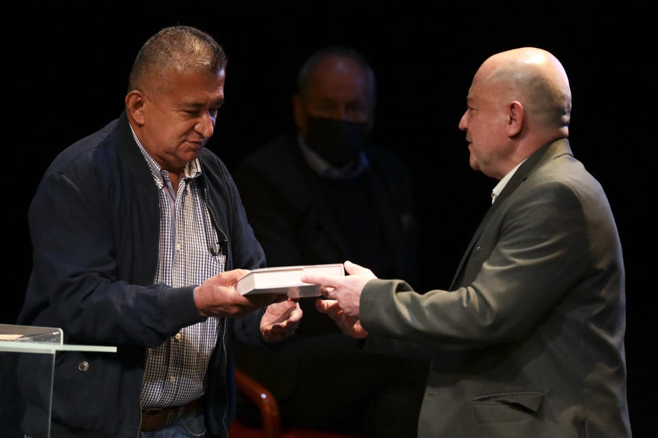 Armando Acuña, left, a former city councilman who was kidnapped by the Revolutionary Armed Forces of Colombia, FARC, is handed a book of the peace accords by former FARC commander Carlos Antonio Lozada, during an event at the Truth Commission to commemorate victims of the country’s decades-long armed conflict, in Bogota, Colombia, Wednesday, June 23, 2021. (AP Photo/Ivan Valencia)