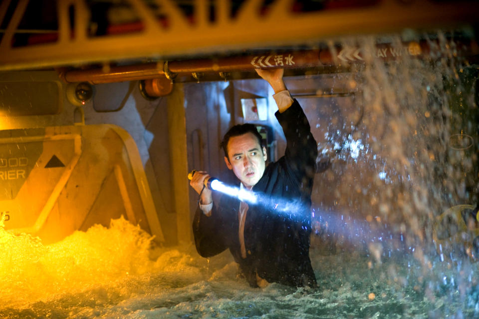 In a scene, John Cusack in a suit clings to a vehicle's underside with a flashlight in water