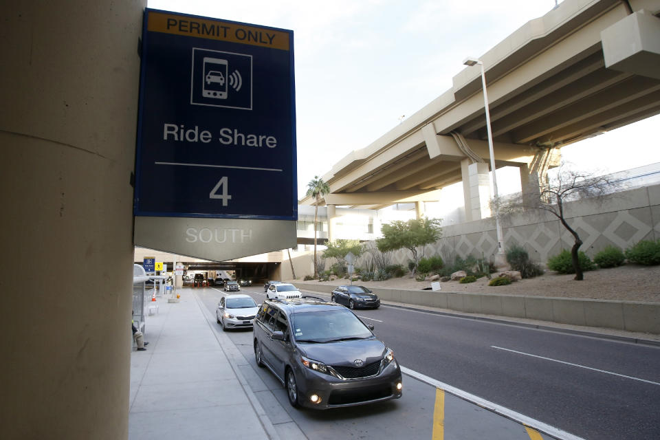 FILE - In this Dec. 18, 2019, file photo passengers find their rides at the Ride Share point as they exit Phoenix Sky Harbor International Airport in Phoenix. The Arizona Supreme Court has unanimously ruled that the Phoenix airport can raise fees for Uber and Lyft to pick up and drop off customers. The ride-hailing companies have threatened to stop serving the airport over the $4 pickup and drop-off fees. The court on Thursday, April 2, 2020 rejected a complaint filed by Republican Attorney General Mark Brnovich, who said the fee hikes are "very likely" unconstitutional. (AP Photo/Ross D. Franklin, File)