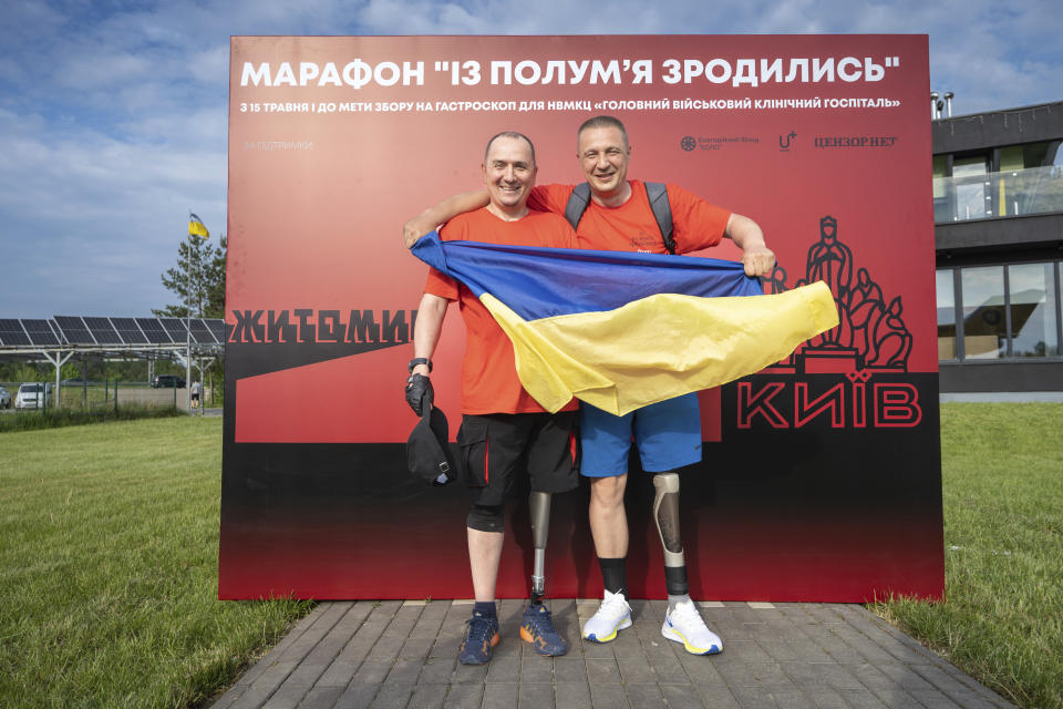 Serhii Khrapko, left, and Oleksandr Shvetsov, both Ukrainian war veterans from 2014, display the Ukrainian flag after successfully completing a 120-kilometer (75-mile) walk to raise money for medical equipment in honor of their comrades wounded in Russia's war against their homeland, in Yuriv, Zhytomyr region, Ukraine, on Friday, May 19, 2023. They raised 3.1 million hryvnias ($84,000), short just the 500,000 hryvnias ($14,000) needed to purchase a new gastroscope for Ukraine's National Military Medical Clinical Center. (AP Photo/Roman Hrytsyna)