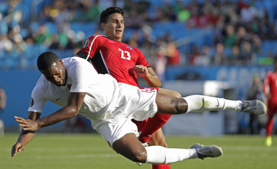 Canada's Doneil Henry, left, dives past Cuba's Luis Paradela (23) during the first half of their CONCACAF Golf Cup soccer match in Charlotte, N.C., Sunday, June 23, 2019. (AP Photo/Chuck Burton)