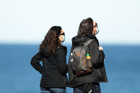 A couple wear face masks while walking at Bondi Beach  in Sydney, Australia. 