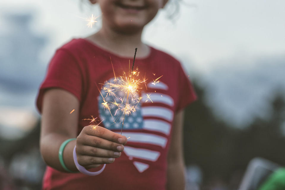 Midsection view of girl holding a lit sparkler with heart-shaped American flag t-shirt on. (Rebecca Nelson / Getty Images)