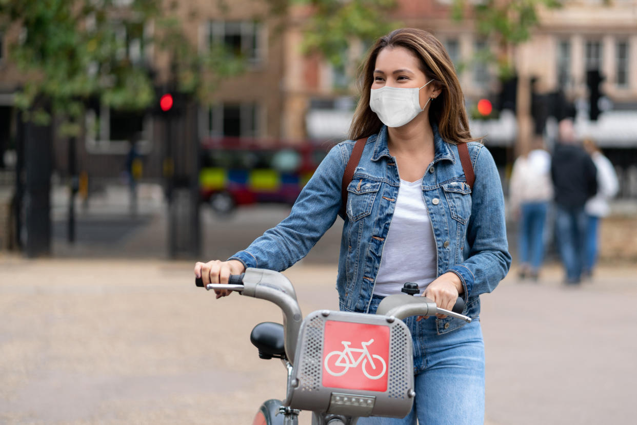 Portrait of a happy woman outdoors wearing a facemask to avoid the spread of coronavirus and renting a bike in London â pandemic lifestyle concepts