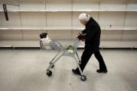 An elderly lady passes empty shelves in Sainsbury's supermarket