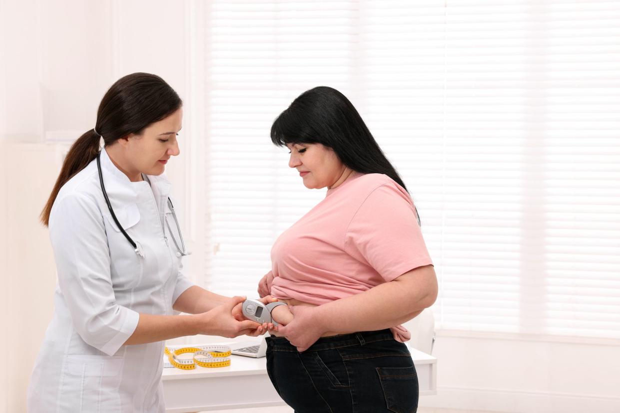 Nutritionist measuring overweight woman's body fat layer with caliper in clinic