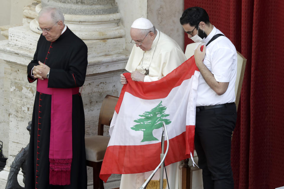Pope Francis is flanked by Lebanese priest Georges Breidi as they hold a Lebanese flag in remembrance of last month's explosion in Beirut, during the pontiff's general audience, the first with faithful since February when the coronavirus outbreak broke out, at the San Damaso courtyard, at the Vatican, Wednesday, Sept. 2, 2020. (AP Photo/Andrew Medichini)