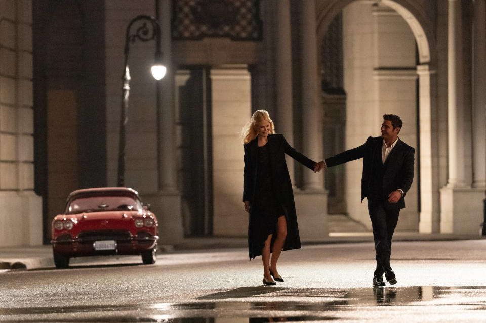 Context from the article suggests the image features Kate Winslet and Hugh Jackman. Both are walking and holding hands at night in an elegant urban setting