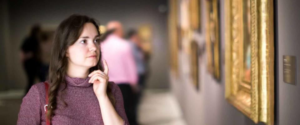 Portrait of positive young girl attentively looking at paintings in art museum