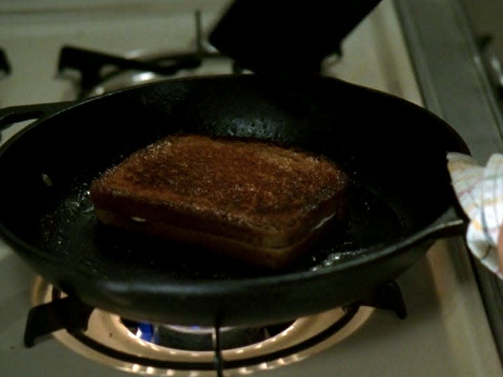 hand holding a cast iron skillet with a cooked grilled cheese inside devil wears prada