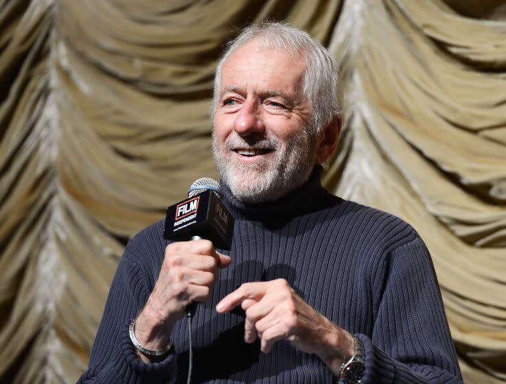 Barry Newman in a black turtleneck holding a microphone in his right hand and smiling
