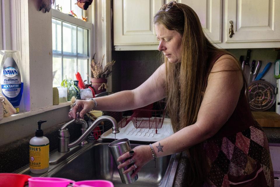 Crystal Dotson fills a cup with tap water in the kitchen of her home in Corinth.