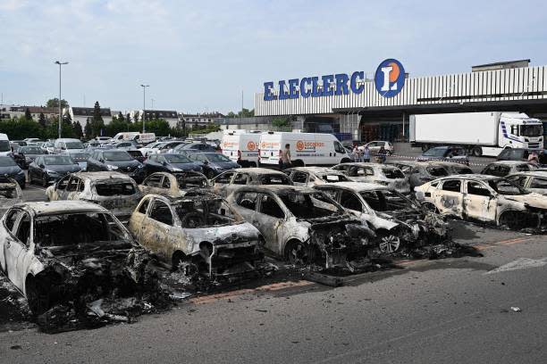 A man walks past burnt out vehicles stationed in the carpark of a supermarket following violence in Schiltigheim, eastern France on 29 June  2023 (AFP via Getty Images)