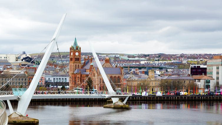 A large white bridge over a grey river with a brick tower in the background.