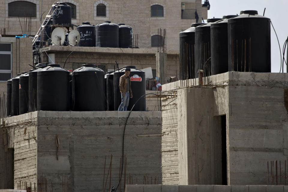 In this April 3, 2014 photo, a Palestinian man walks near water tanks on the roof of a building in Shuafat in east Jerusalem. Tens of thousands of Palestinians in east Jerusalem have been without water for more than a month, victims of a decrepit and overwhelmed infrastructure and caught in a legal no-man’s land. Their district is technically part of Jerusalem municipality, but on the other side of the massive Israeli-built West Bank separation barrier, so Israeli services there are sparse yet Palestinian officials are barred for operating. With the scorching summer approaching, residents are growing increasingly desperate. (AP Photo/Sebastian Scheiner)