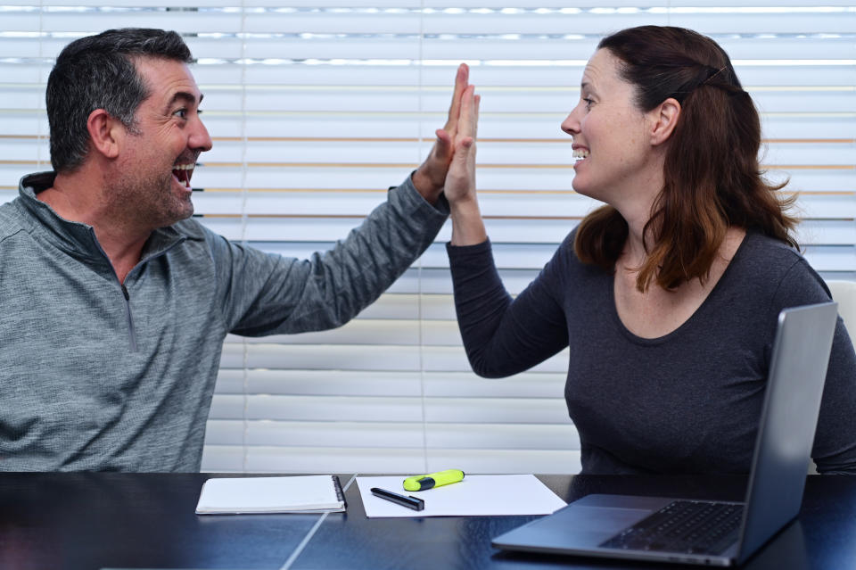 Happy adult couple high five after looking at positive finance data on a laptop.