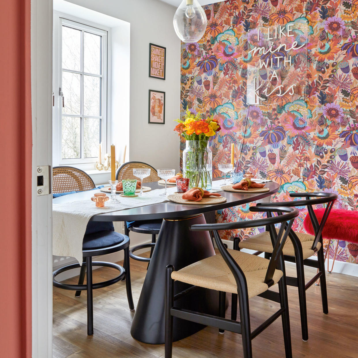  Modern-style dining table with wishbone chairs and floral pink wallpaper. 