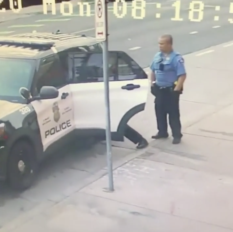 Minneapolis police officers are pictured standing at their police car in CCTV footage.