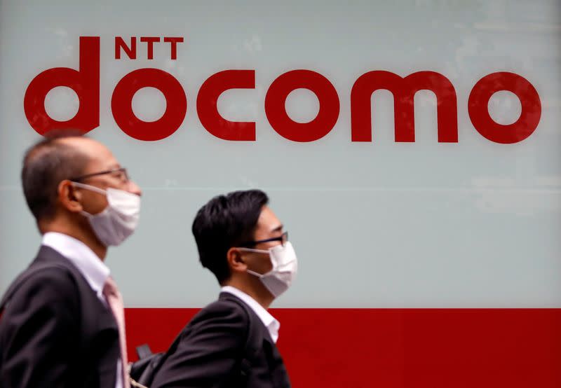 Passersby wearing protective face masks walk past in front of NTT Docomo shop in Tokyo, Japan