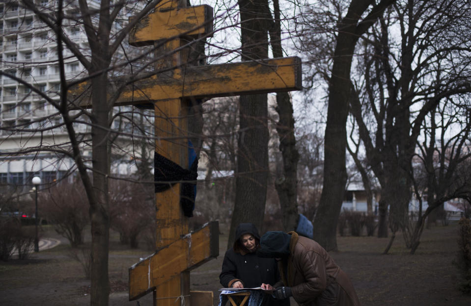 Women read prayers at a cross placed near the Parliament in Kiev Ukraine, Monday, March 17, 2014. Ukraine's political turmoil has become Europe's most severe security crisis in years and tensions have been high since Russian troops seized control of Crimea two weeks ago. (AP Photo/David Azia)