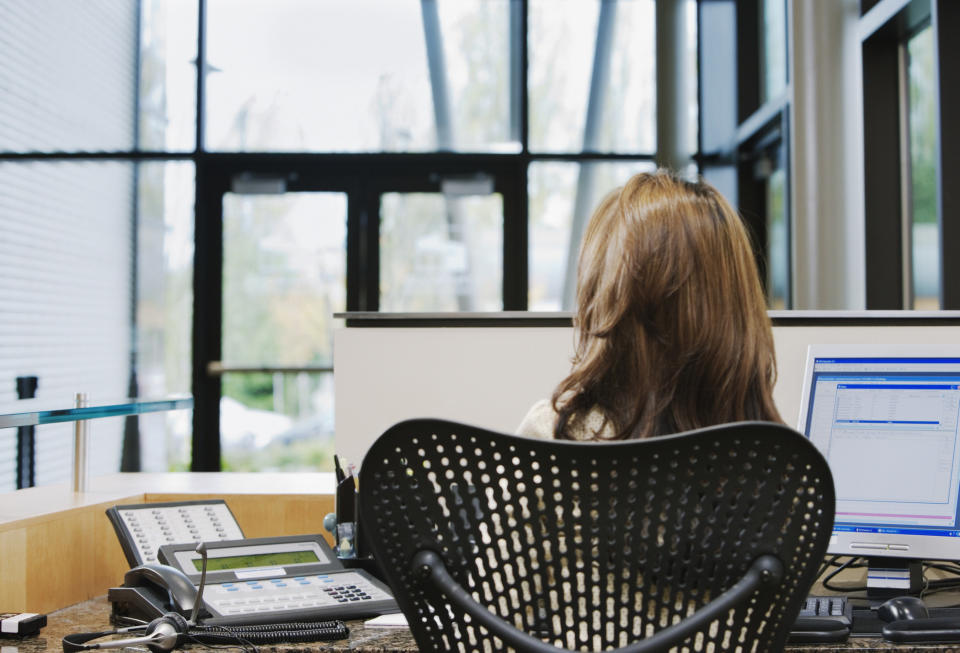 The back of a woman's head as she sits in front of a phone and computer at a desk