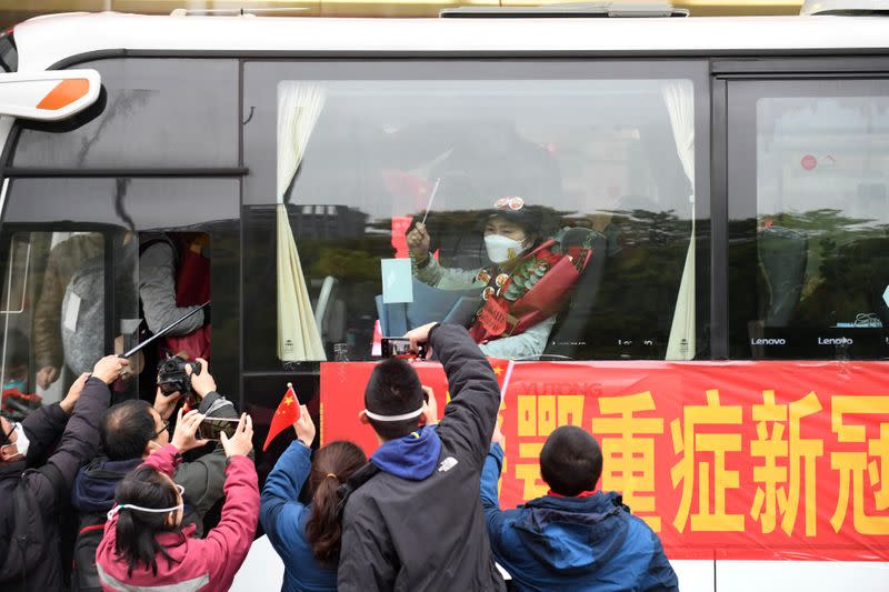 Li Lanjuan waves a Chinese flag from inside a bus as she leaves Wuhan