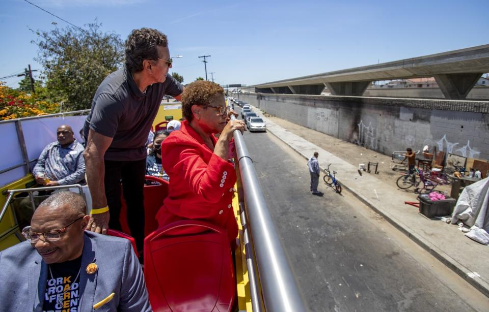 Two people look at a homeless encampment from a double-decker bus.