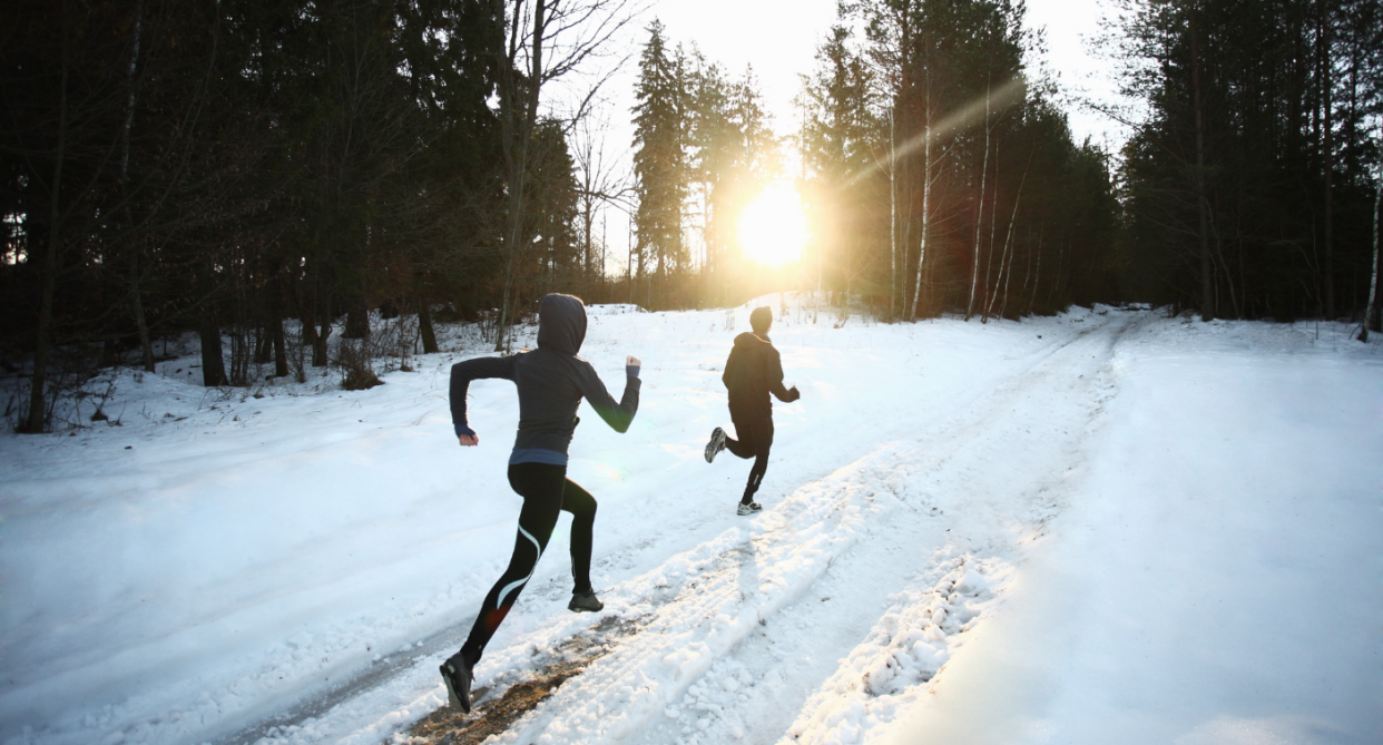 two people running in snow outside on trail, winter running, winter running shoes, people running in forest outside during winter, Shopping for winter running shoes? Here's what you need to know (Photos via Getty)