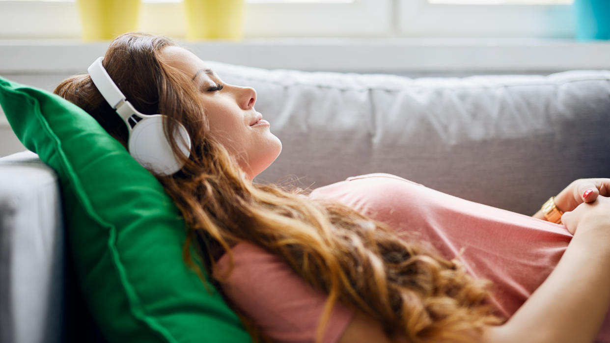 Portrait of a beautiful young woman lying on sofa with headphones on and closed eyes, relaxing.