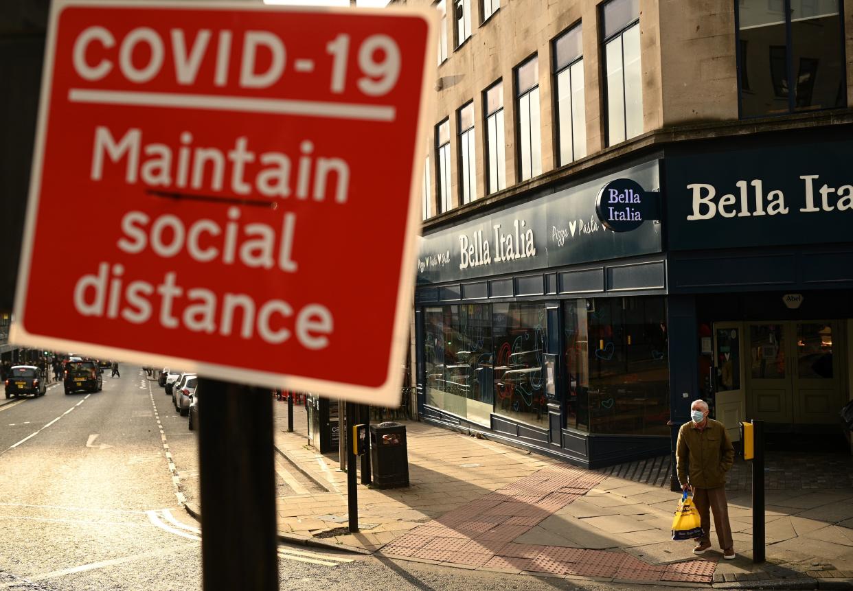 A man wearing a face mask or covering due to the COVID-19 pandemic, stands at a road crossing near a sign alerting pedestrians to social distance to help mitigate the spread of COVID-19 in Liverpool, north west England on October 2, 2020, following the  announcement of new local restrictions for certain areas in the northwest of the country, due to a resurgence of novel coronavirus cases. - The British government on Thursday extended lockdowns to Liverpool and several other towns in northern England, effectively putting more than a quarter of the country under tighter coronavirus restrictions. Health Secretary Matt Hancock said limits on social gatherings would be extended to the Liverpool City region, which has a population of about 1.5 million. (Photo by Oli SCARFF / AFP) (Photo by OLI SCARFF/AFP via Getty Images)