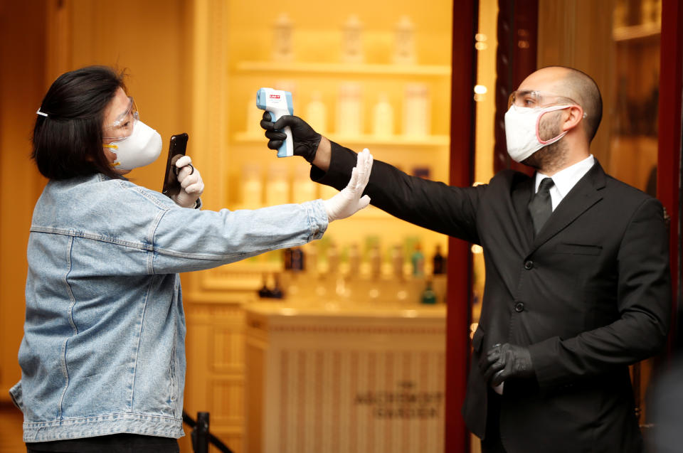 A woman has her temperature checked before entering a shop.