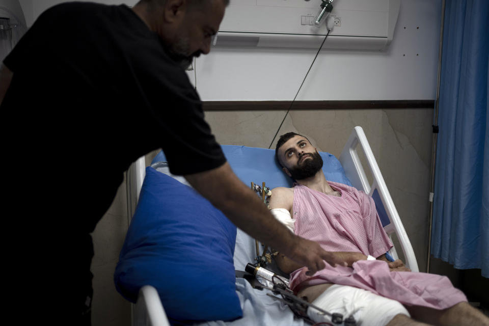 Raed Abadi, left, tends to his son, Mujahid Abadi, 24, as he recovers from gunshot wounds and burns at the Ibn Sina Specialized Hospital in the West Bank city of Jenin, Tuesday, June 25, 2024. When the Palestinian man stepped outside to see if Israeli forces had entered his uncle's neighborhood, he was shot in the arm and the foot. That was only the start of his ordeal. Hours later, beaten and bloodied, he found himself strapped to the searing hood of an Israeli military jeep driving down a road. (AP Photo/Maya Alleruzzo)
