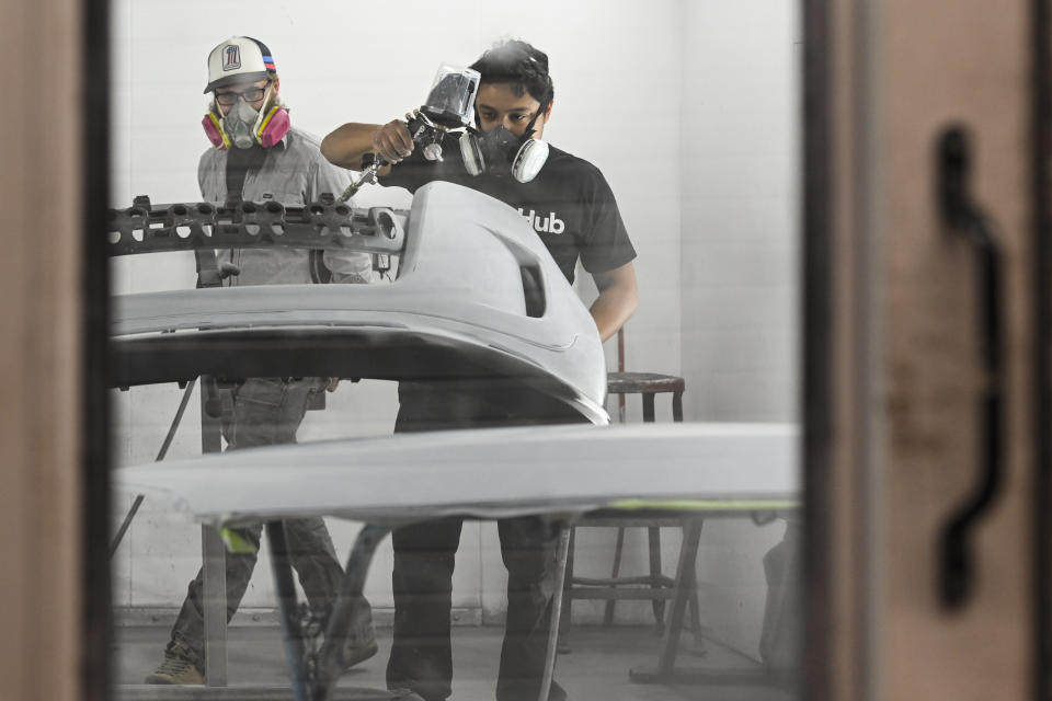 Student Conception Garcia paints a car part under the watchful eye of instructor Austin Monchilov, left, during auto collision repair class at Tennessee College of Applied Technology Nashville Wednesday, April 13, 2023, in Nashville, Tenn. While almost every sector of higher education is seeing fewer students registering for classes, many trade school programs are booming with young people who are choosing trade school over a traditional four-year degree. (AP Photo/John Amis)