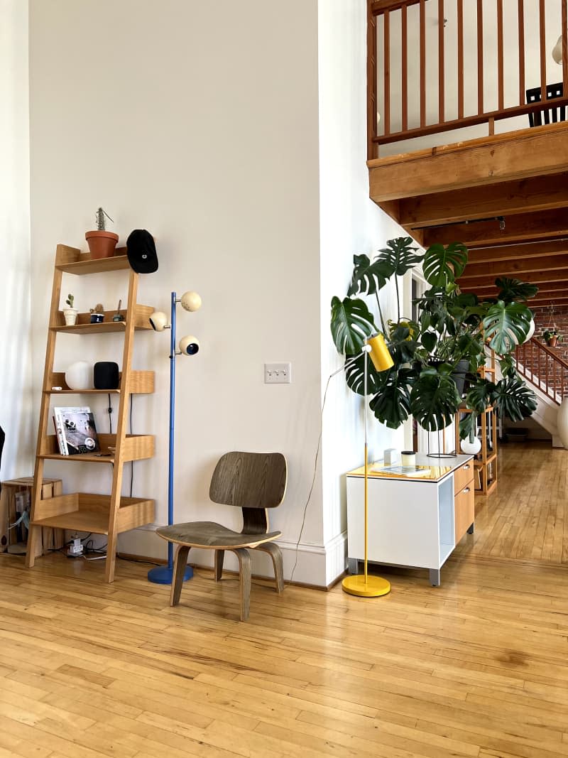 Ladder bookcase and chair against neutral wall of loft with hardwood floor.