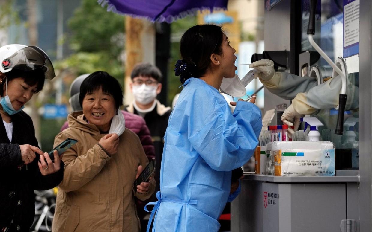 A woman removes her mask at a Covid testing station in Shanghai - ALY SONG/REUTERS