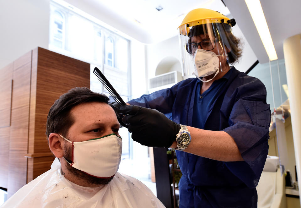 A hairdresser treats a customer while both wear protective masks.
