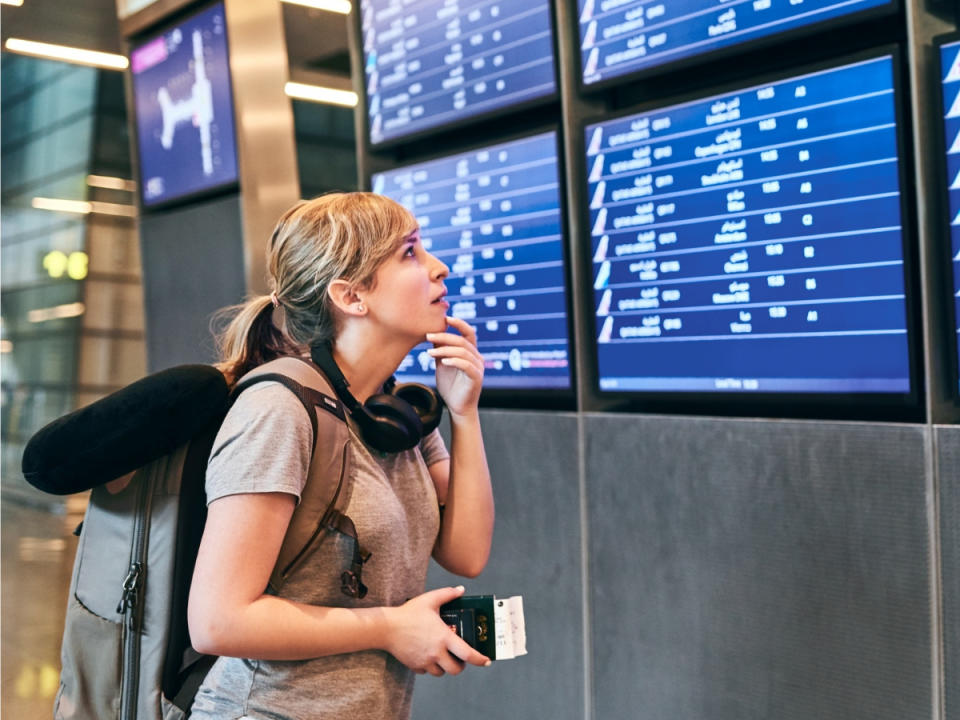 An attractive young woman with a passport looking at the flight schedule in an airport. (Source:Getty)