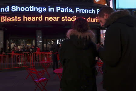 People watch as a news ticker updates people with the news of the shooting attacks in Paris, in Times Square in the Manhattan borough of New York November 13, 2015. REUTERS/Carlo Allegri