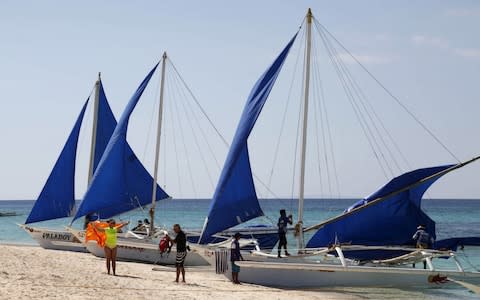 Tourists takes photographs along local sailboats on the island of Boracay, central Philippines - Credit: Reuters