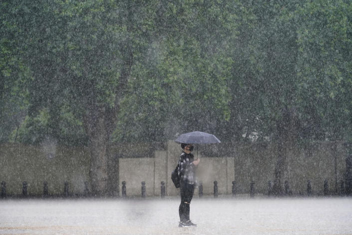 A woman stands in the rain in Horse Guards Parade in central London, Sunday July 25, 2021. Thunderstorms bringing lightning and torrential rain to the south are set to continue until Monday it is forecast. (Victoria Jones/PA via AP)