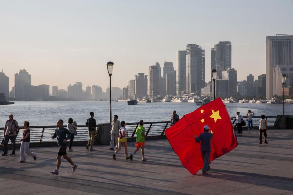 Ein Mann, der einen Drachen in Form der chinesischen Nationalflagge trägt, spaziert an der Uferpromenade des Huangpu-Flusses in Shanghai entlang – gegenüber der Pudong-Finanzbezirks Lujiazui.  - Copyright: Eine chinesische Flagge weht über Shanghai.